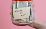 A jar filled with cash and a travel note against a pink backdrop symbolizing savings.