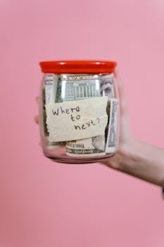 A jar filled with cash and a travel note against a pink backdrop symbolizing savings.