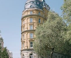 Vertical shot of Corinthia Hotel showcasing London's historic architecture and vibrant city life.