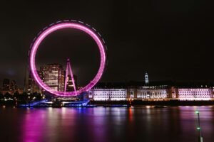 Stunning night view of the London Eye illuminated in pink along the Thames River in London, UK.