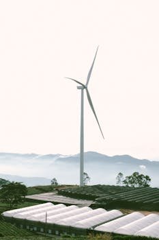 A wind turbine stands tall against mountains and farm fields, symbolizing sustainable energy.