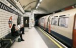 Commuters waiting at Leicester Square station with a train passing by.