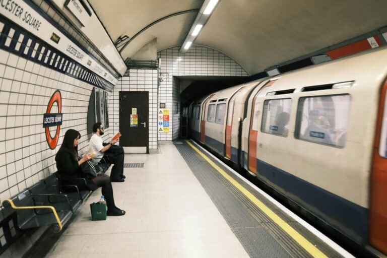 Commuters waiting at Leicester Square station with a train passing by.