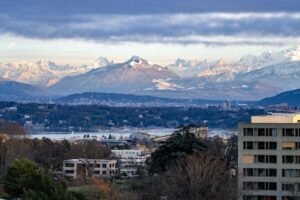 A breathtaking view of Geneva with Swiss Alps backdrop under a cloudy sky at day.