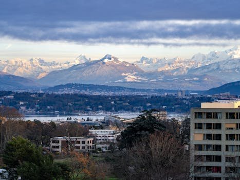 A breathtaking view of Geneva with Swiss Alps backdrop under a cloudy sky at day.