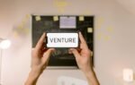 A smartphone displaying 'Venture' held by hands in an office setup. Ideal for business and startup themes.
