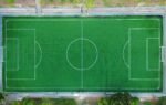 Bright aerial shot of an empty green soccer field with clearly marked lines.