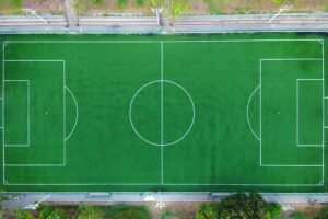 Bright aerial shot of an empty green soccer field with clearly marked lines.
