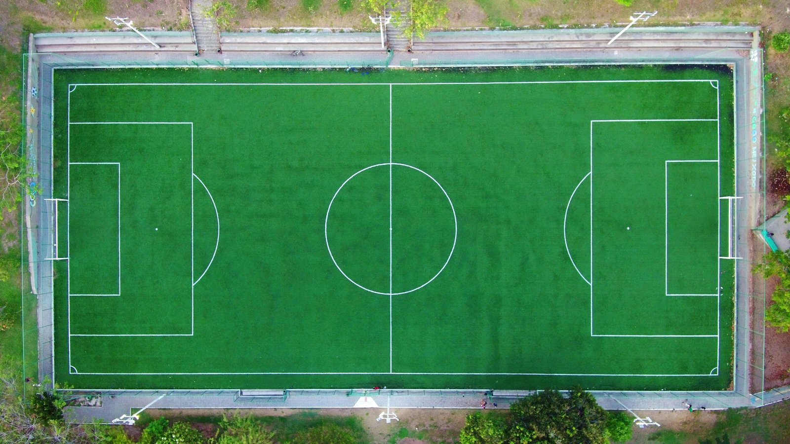 Bright aerial shot of an empty green soccer field with clearly marked lines.
