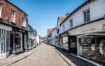 Picturesque view of an empty street in historic Godalming, England with old shops and blue sky.