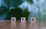 Scrabble tiles spelling ETF on a wooden surface with blurred green background.