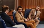 Three businessmen seated in a stylish conference room engaged in discussion.