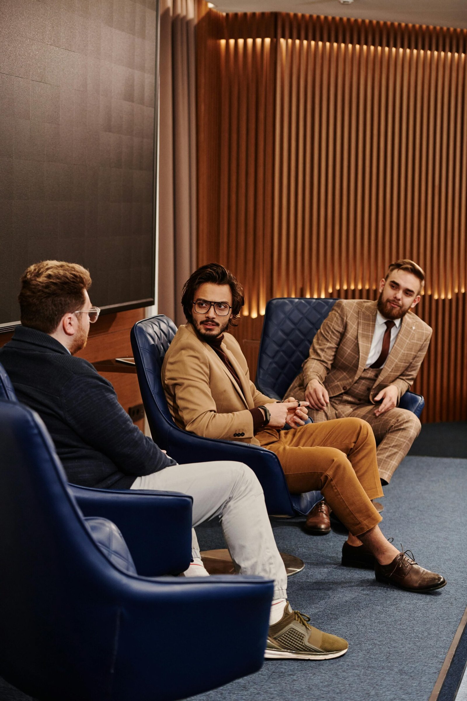 Three businessmen seated in a stylish conference room engaged in discussion.